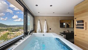 A modern bathroom with a large bathtub, a sink, and a mirror. There is a window with a view of a town and mountains. - L'Eden Bleu in Langlade, upscale romantic suite with private SPA. (Langlade)