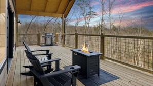 Eine überdachte Terrasse mit Grill und Feuerstelle, mit Blick auf einen bewaldeten Bereich.