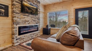 Ein gemütliches Wohnzimmer mit Kamin aus Stein, einer Ledersofa und einem großen Fenster mit Jalousien.