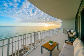 A balcony with a view of the sea and sunset, featuring a sofa, a small table, and a potted plant. - Phoenix Gulf Shores Ii 1105 4 Bedroom Condo (Gulf Shores)