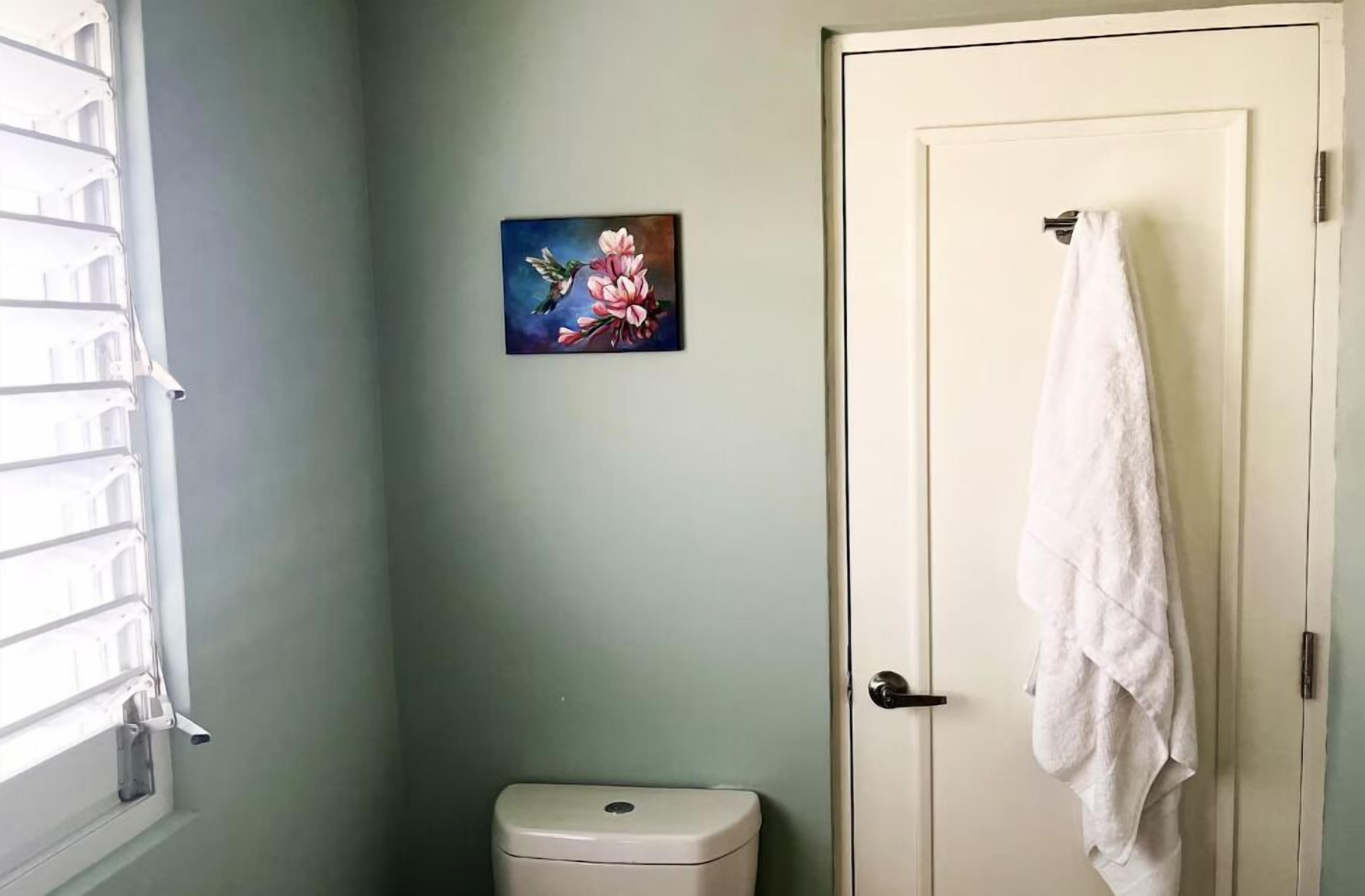 Un bagno con un WC, un asciugamano appeso alla porta e un quadro con dei fiori al muro.