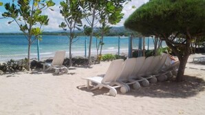 A beach with white lounge chairs arranged in rows, a tree providing shade, and a view of the sea. - The Crest - Serenity Oasis Villa (St. Ann's Bay)