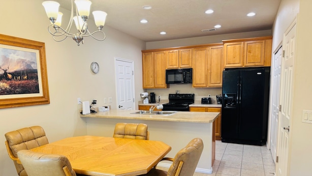 A kitchen with wooden cabinets, a black refrigerator, a microwave, and a sink. There is a dining table with chairs and a chandelier. - Juniper Retreat | Ground 2BR Pet-Friendly + over $500 in complimentary activities! (Mesquite)