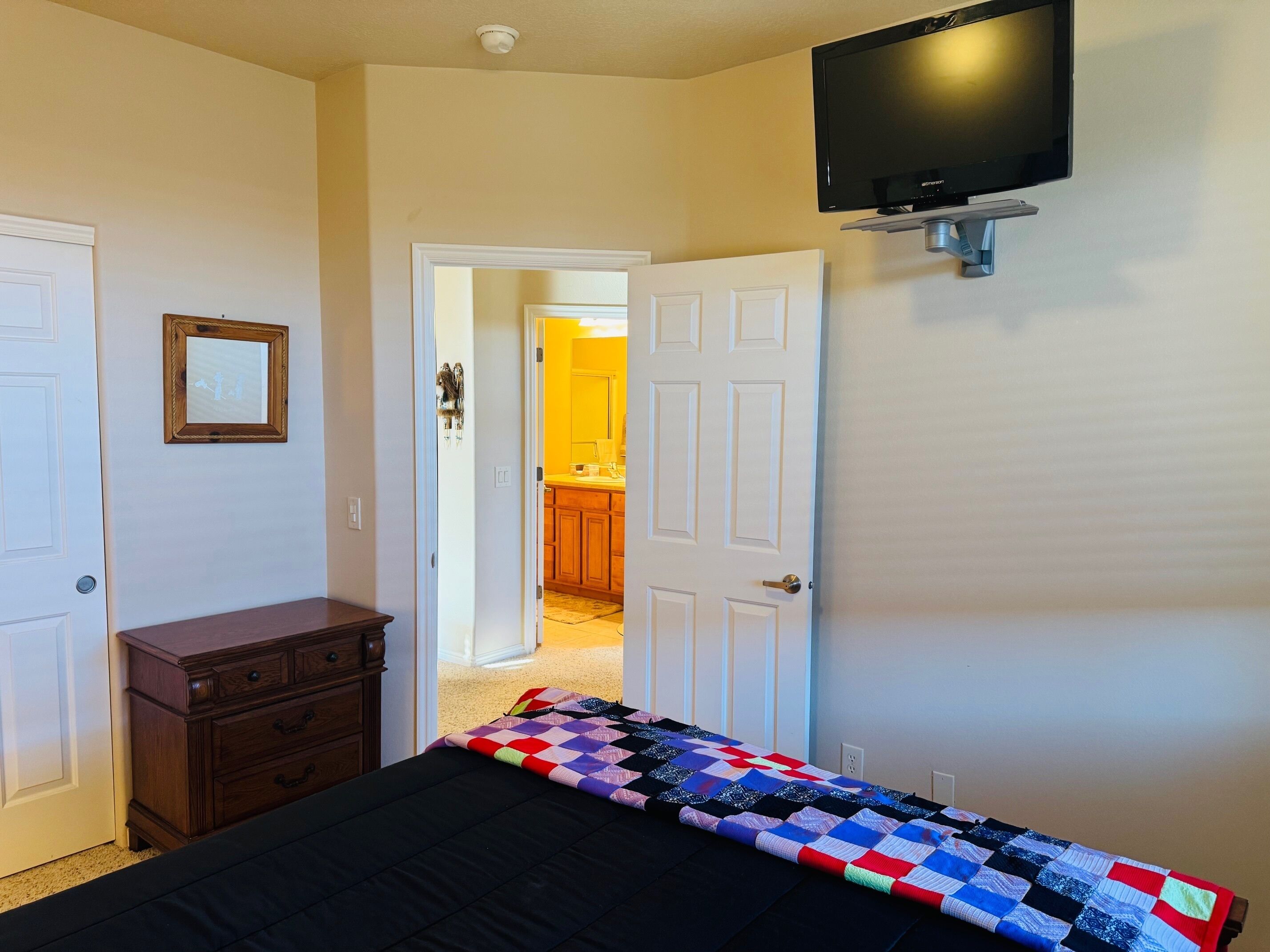 A bedroom with a bed, dresser, and a TV mounted on the wall.
