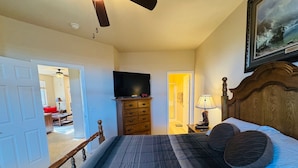A bedroom with a bed, wooden headboard, a dresser, a television, and a painting on the wall. - Juniper Retreat | Ground 2BR Pet-Friendly + over $500 in complimentary activities! (Mesquite)