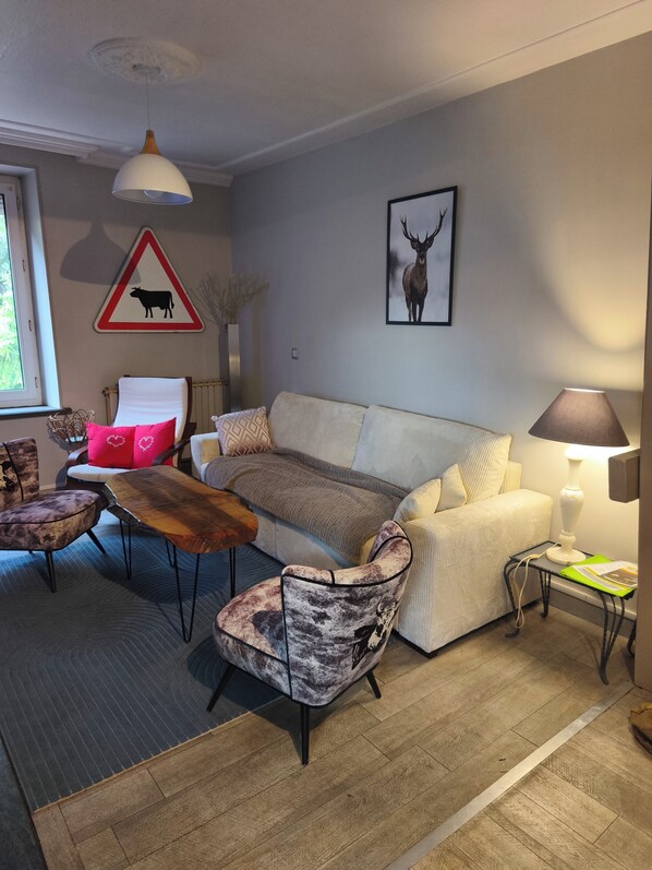 Un salon comprenant un canapé, des fauteuils, une table basse, une lampe, un tableau représentant un cerf encadré et un panneau de signalisation routière.