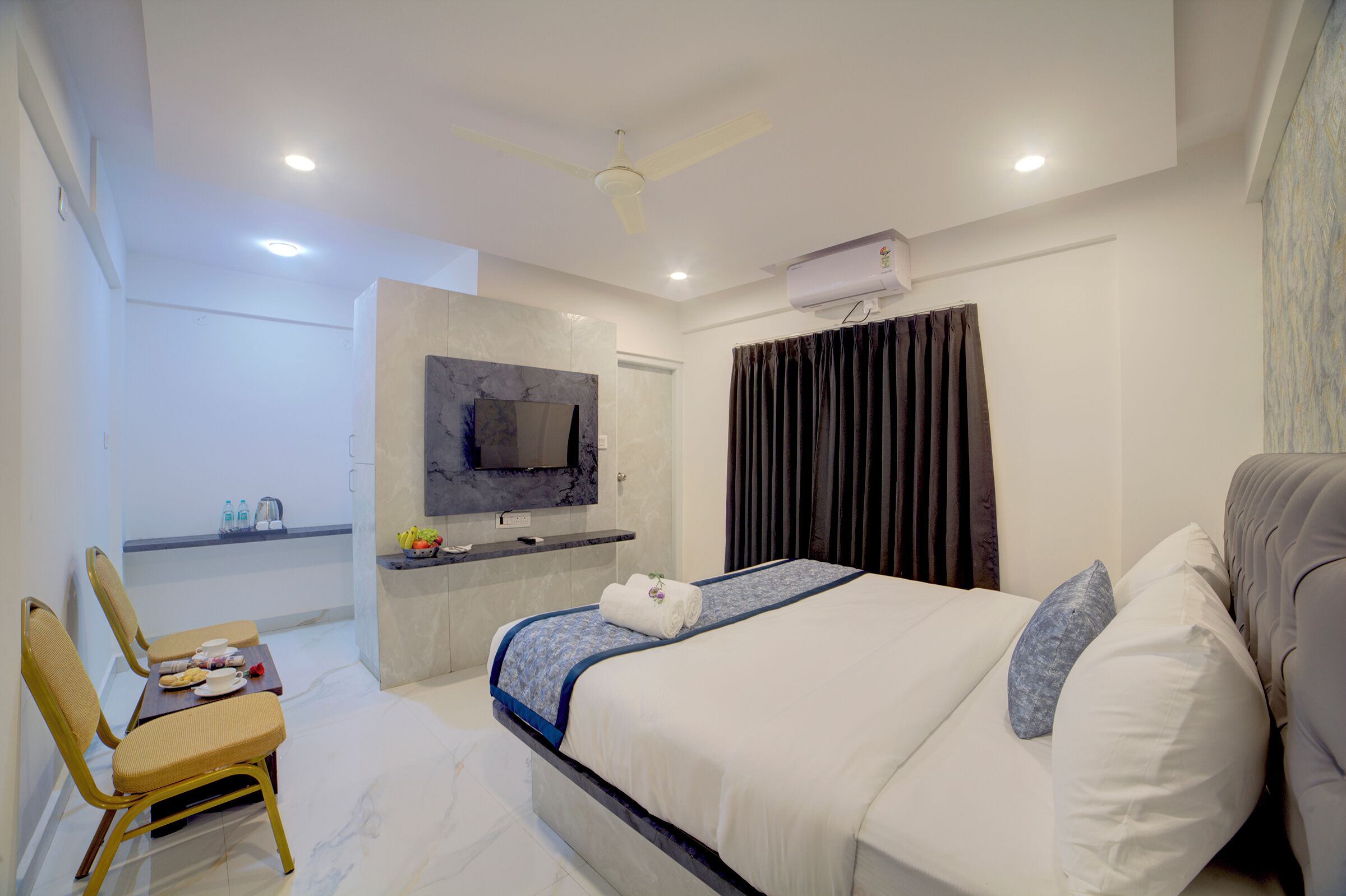 A modern hotel room with a bed, a desk with a flat-screen TV, a ceiling fan, and an air conditioning unit.