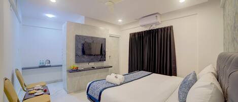 A modern hotel room with a bed, a desk with a flat-screen TV, a ceiling fan, and an air conditioning unit.