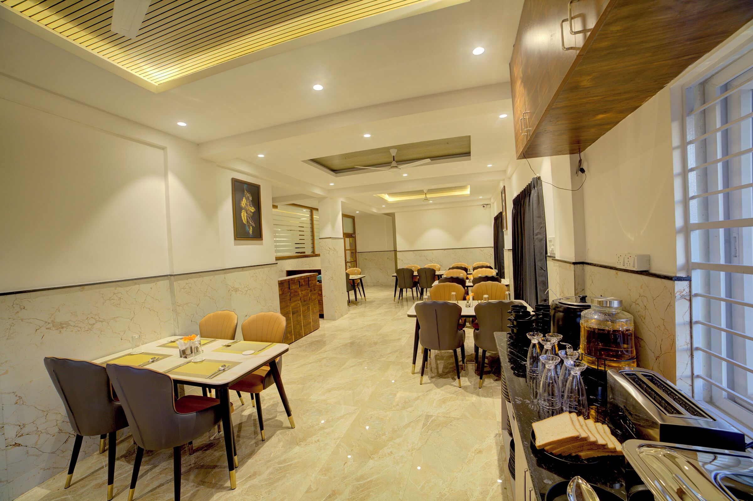 A spacious dining area with multiple tables and chairs, a buffet setup with various food items, and a ceiling fan.