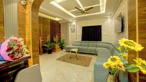 A modern living room with a sectional sofa, a coffee table, and a decorative vase with sunflowers. - Hotel AeroStay Bangalore Airport (Bangalore)