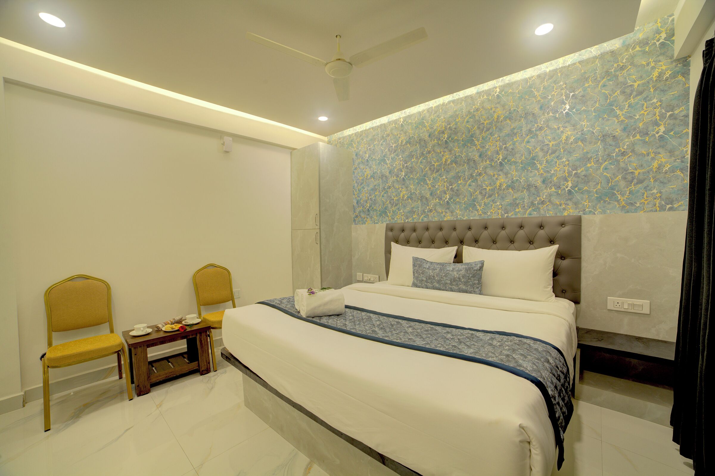 A neatly arranged bedroom with a bed, two chairs, a small table, and a ceiling fan.