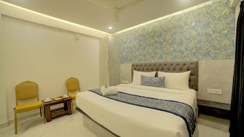 Un dormitorio ordenado con una cama, dos sillas, una mesita y un ventilador de techo.