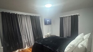Une chambre avec un plancher en bois, un lit avec une literie blanche et un téléviseur fixé au mur.