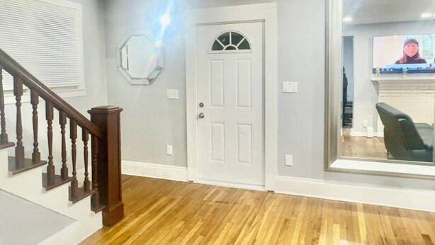 Un hall d’entrée spacieux avec un plancher en bois, une porte blanche et un escalier doté de rampes en bois.