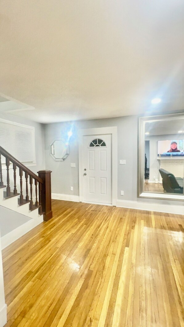 Un hall d’entrée spacieux avec un plancher en bois, une porte blanche et un escalier doté de rampes en bois.