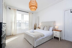 A bedroom with a bed, bedside tables, a dresser, and a window with curtains. - Bright 4-Bedroom Maisonette Family & Work Stays (Gateshead)
