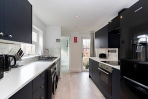 A modern kitchen with black cabinets, a built-in oven, and a coffee machine. - Bright 4-Bedroom Maisonette Family & Work Stays (Gateshead)