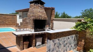 A brick-built outdoor kitchen with a chimney, adjacent to a swimming pool and a tiled patio area. - Villa Villa Maria 10 min. from Puy Du Fou. Ideal for families and groups of friends (CM)