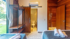 A room with a bed, a wooden wardrobe, a shelf, and a bathroom visible through an open door. - Well-located Condominium in Campinhos in Maraú - RVEs (Maraú)