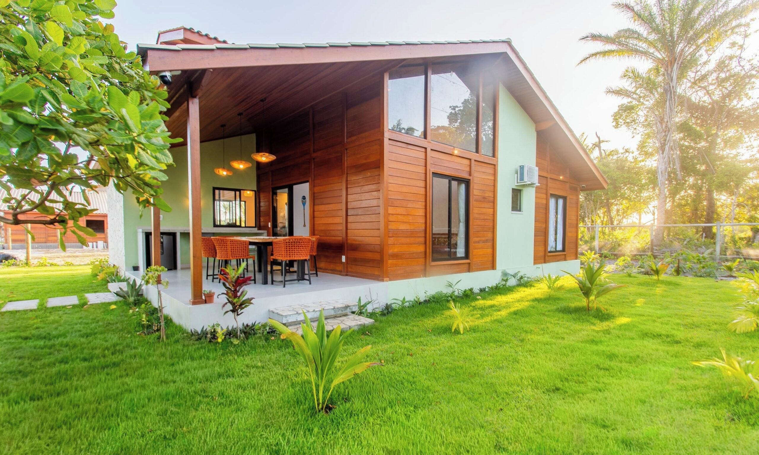 A modern house with a covered porch, a dining area with chairs, and a well-maintained lawn.