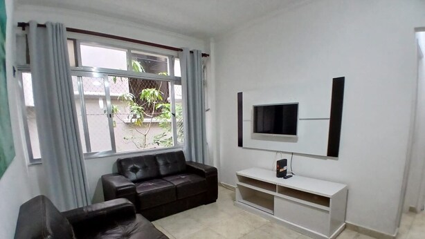Ein Wohnzimmer mit einem dunkelbraunen Sofa, einer weißen TV-Konsole und einem Fenster mit Vorhängen.