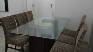Ein Essbereich mit einem Glastisch, vier gestreiften Stühlen, einem gerahmten Bild an der Wand und einer weißen Tür im Hintergrund.