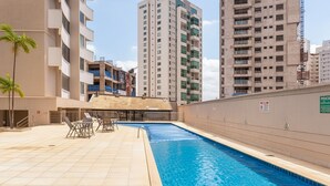 A swimming pool with lounge chairs, a covered seating area, and high-rise buildings in the background. - 2brs apt 950 m fr/ Flamboyant Mall Unq1104 (Goiânia)