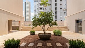 A courtyard with a central tree, surrounded by potted plants and a stone pathway. - 2brs apt 950 m fr/ Flamboyant Mall Unq1104 (Goiânia)