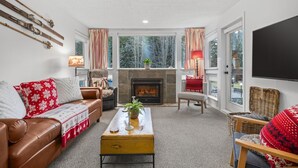 Un salon chaleureux avec une cheminée, un canapé en cuir et une grande fenêtre agrémentée de rideaux.