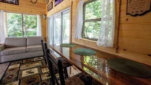 L’intérieur chaleureux d’un chalet avec un canapé, une table à manger, des chaises et de grandes fenêtres donnant sur le paysage extérieur.