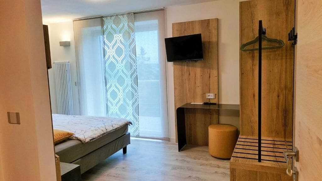 A modern bedroom with a bed, a TV mounted on the wall, a wooden wardrobe, and a hanging clothes rack.