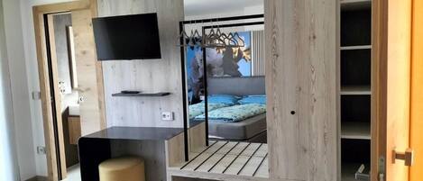 A modern bedroom with a TV mounted on the wall, a bed with a blue headboard, and a wooden wardrobe with a mirror.