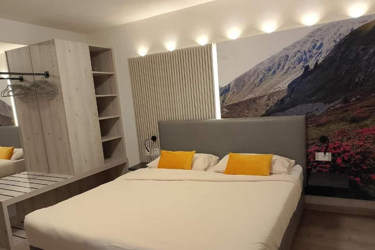 A bedroom with a bed, a wooden wardrobe, a shelf unit, and a large mountain landscape mural on the wall.