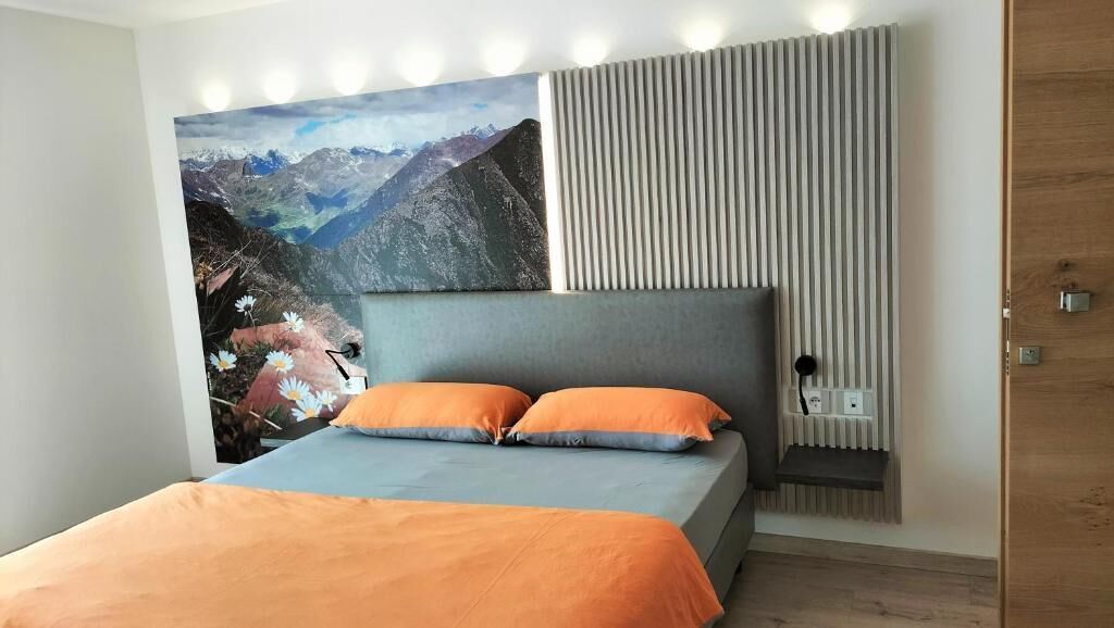A modern bedroom with a large bed, a mountain landscape painting, a slatted wall, and a wooden door.
