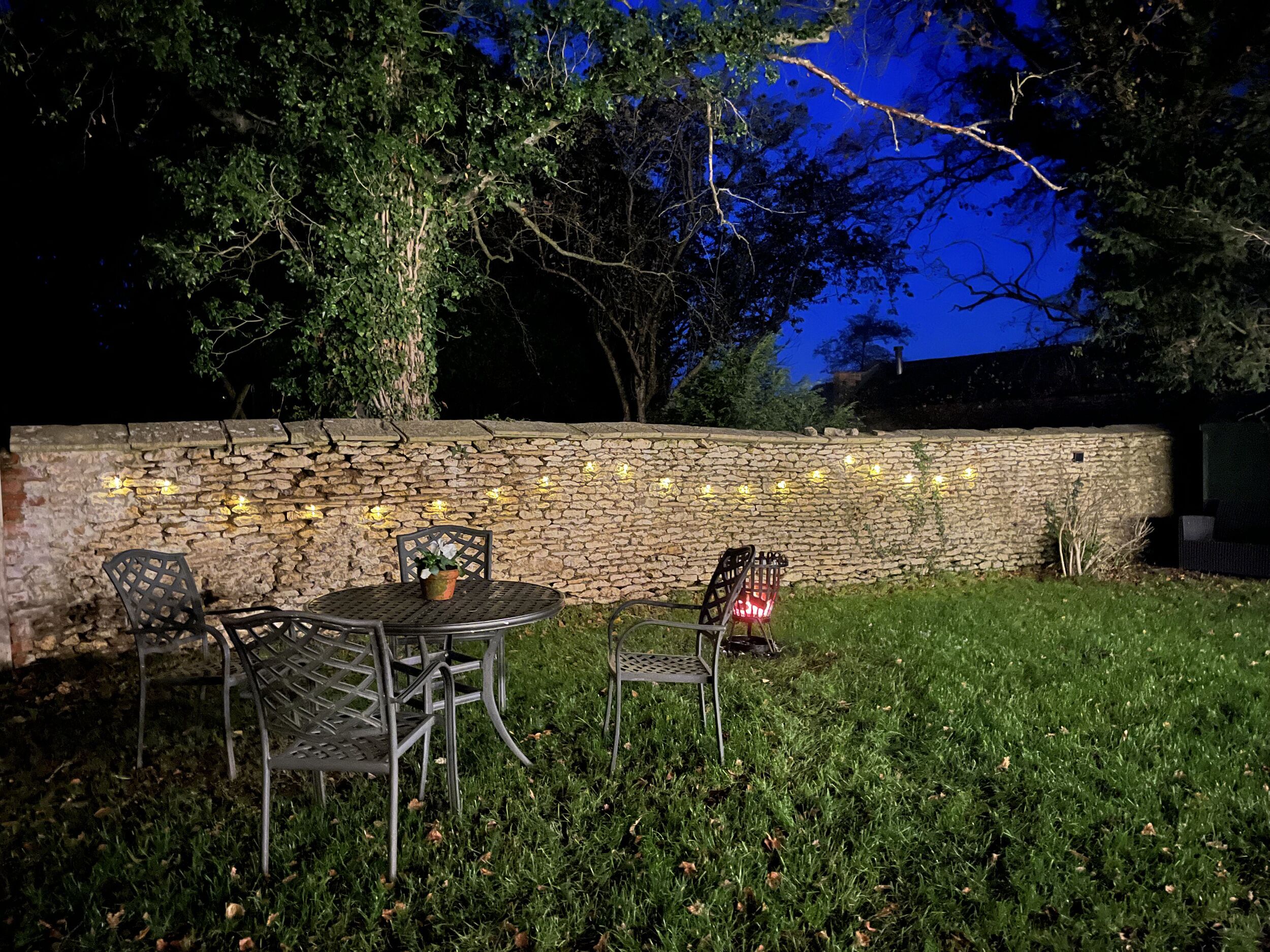 Un espacio al aire libre con pared de piedra, sillas de metal y una mesa.