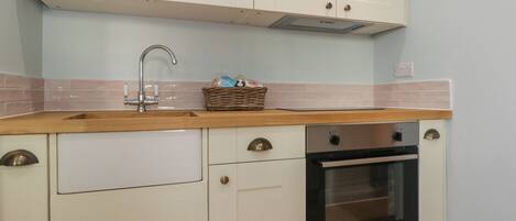 A kitchen with white cabinets, a wooden countertop, a stainless steel oven, and a sink.