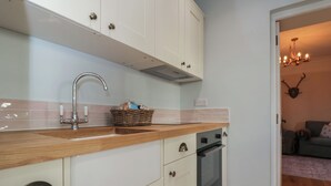 Una cocina con armarios blancos, encimera de madera, pileta de acero inoxidable y horno.