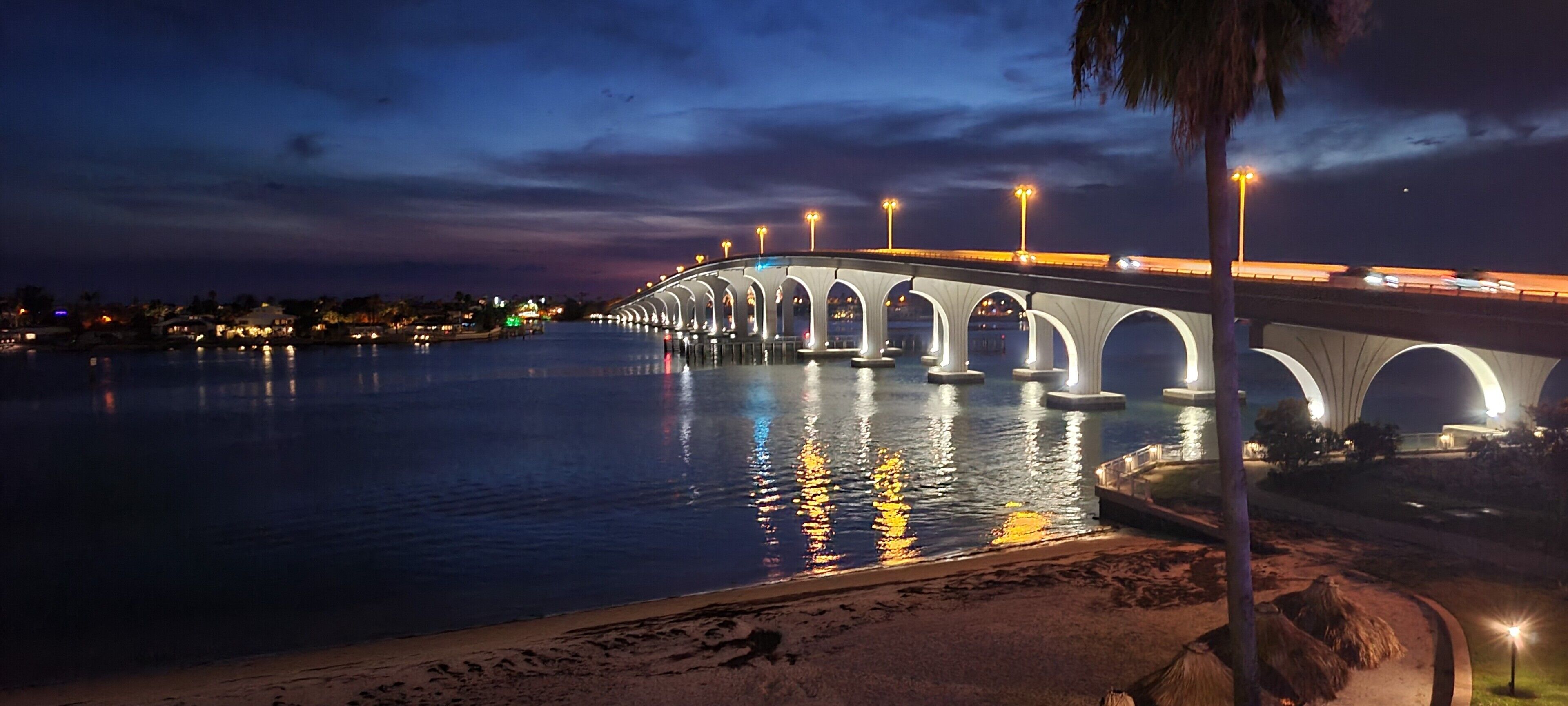 A bridge with multiple arches over a body of water, illuminated by street lights.