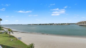En strand med fri utsikt över havet, en sandstrand och en avlägsen stadsbild med byggnader och en bro.
