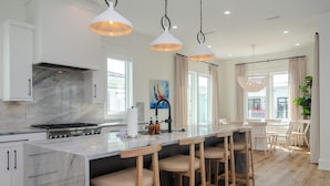 A modern kitchen with a marble countertop, bar stools, pendant lights, and a view of the outside. - Stunning Custom Home with Pool & Rooftop Deck (Wrightsville Beach)