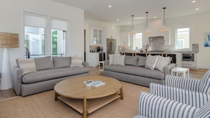 A modern living room with two grey sofas, a round coffee table, and striped armchairs. - Stunning Custom Home with Pool & Rooftop Deck (Wrightsville Beach)