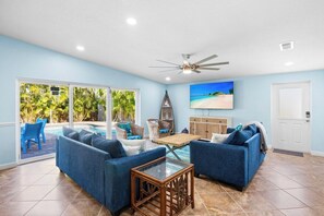A living room with a pool view, blue sofas, and a ceiling fan. - Wonderful 3/2 close to beach! Heated pool! (Holmes Beach)