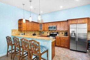 A kitchen with wooden cabinets, a stainless steel refrigerator, and a central island with bar stools. - Wonderful 3/2 close to beach! Heated pool! (Holmes Beach)