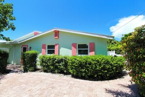A two-story house with a green facade and pink shutters, surrounded by well-maintained hedges. - Wonderful 3/2 close to beach! Heated pool! (Holmes Beach)