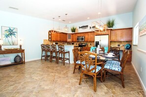A spacious kitchen with wooden cabinets, a microwave, and a dining area with wicker chairs and a blue and white patterned tablecloth. - Wonderful 3/2 close to beach! Heated pool! (Holmes Beach)