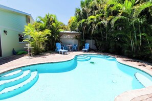 A swimming pool with blue chairs and a covered seating area surrounded by lush greenery. - Wonderful 3/2 close to beach! Heated pool! (Holmes Beach)