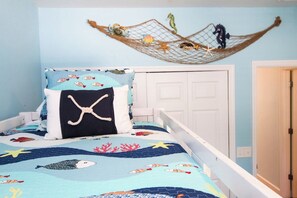 Een slaapkamer met een bed, voorzien van een beddegoed met nautisch thema, een decoratief net met vissen en een zeepaardje, en een witte deur op de achtergrond.