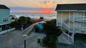 Vista costera con un atardecer sobre el océano, una piscina y edificios frente a la playa.