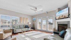 Un salón espacioso con chimenea, ventilador de techo y ventanas amplias.
