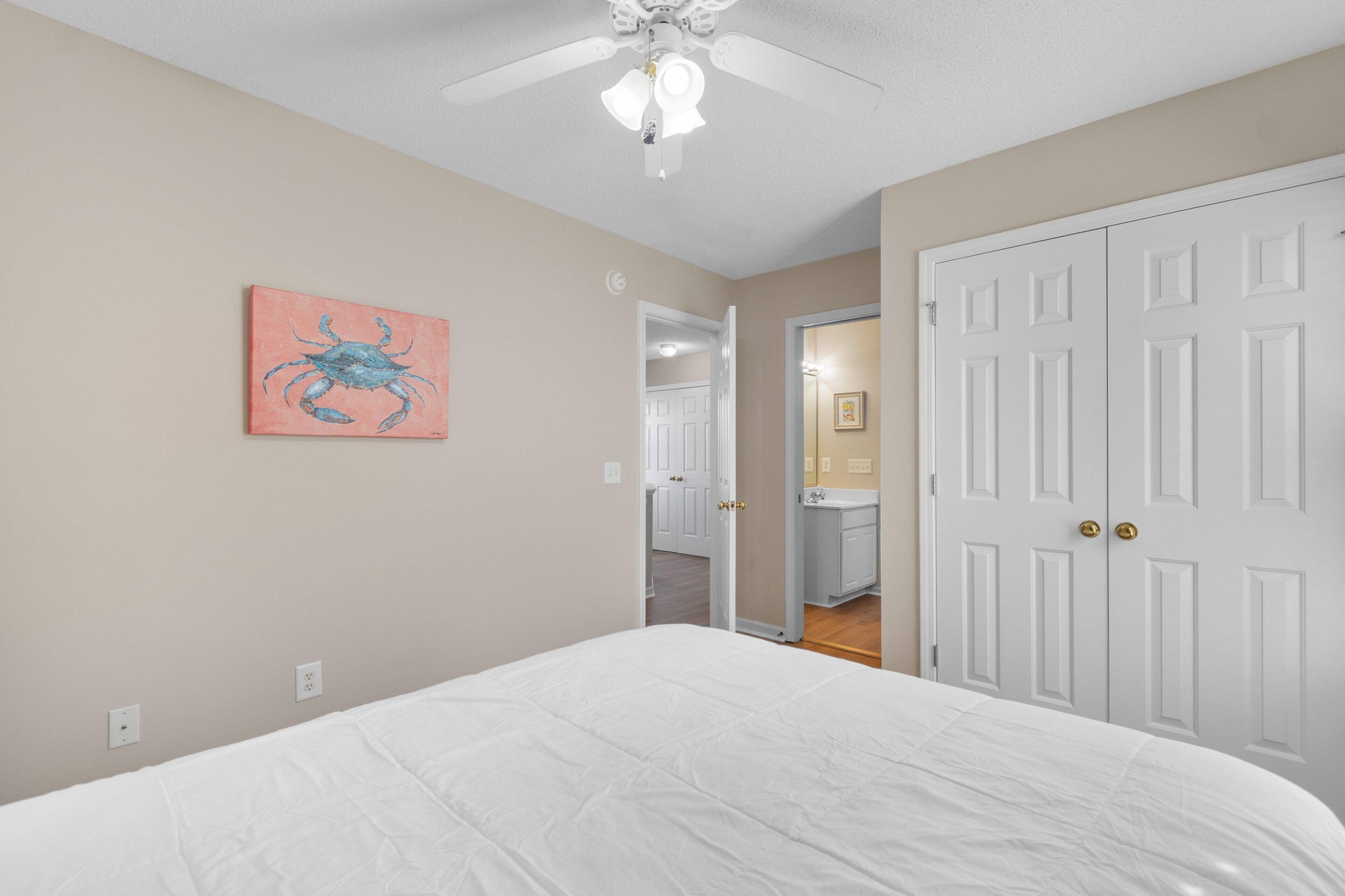 A bedroom with a bed, a ceiling fan, a door, and a hallway leading to a bathroom.